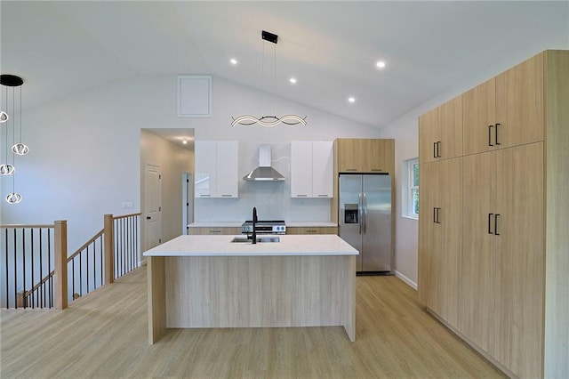 kitchen with white cabinets, a center island with sink, wall chimney range hood, hanging light fixtures, and appliances with stainless steel finishes