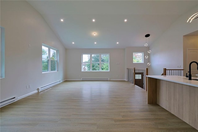 unfurnished living room with baseboard heating, a wealth of natural light, and light hardwood / wood-style flooring