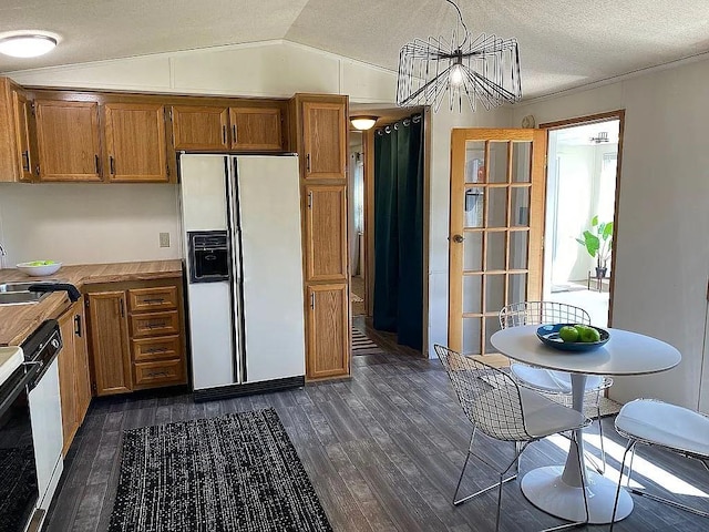 kitchen featuring pendant lighting, lofted ceiling, white appliances, dark wood-type flooring, and a textured ceiling