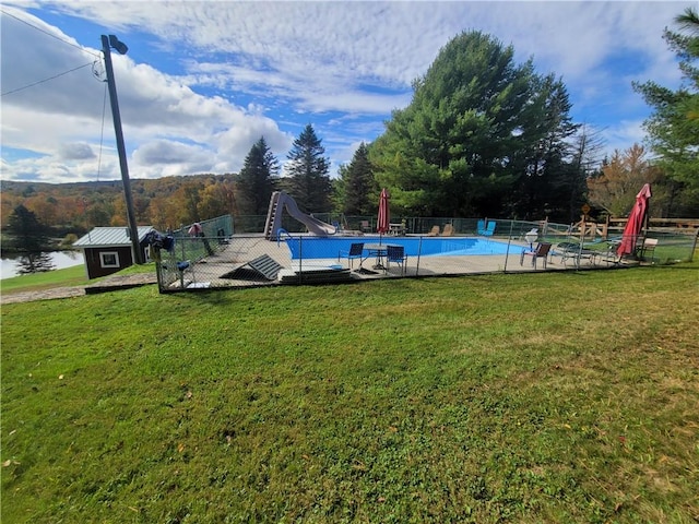 view of swimming pool featuring a water view, a lawn, an outdoor structure, and a water slide