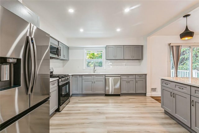 kitchen featuring decorative light fixtures, a healthy amount of sunlight, appliances with stainless steel finishes, and light hardwood / wood-style flooring