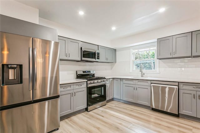 kitchen with stainless steel appliances, gray cabinets, light hardwood / wood-style floors, and sink