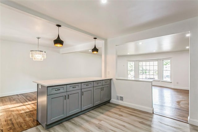 kitchen featuring pendant lighting, an inviting chandelier, light hardwood / wood-style flooring, gray cabinets, and kitchen peninsula