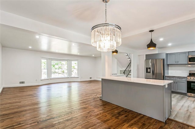kitchen featuring dark wood-type flooring, gray cabinets, decorative light fixtures, a kitchen island, and stainless steel appliances
