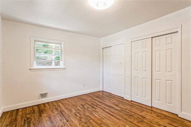 unfurnished bedroom with two closets and dark wood-type flooring