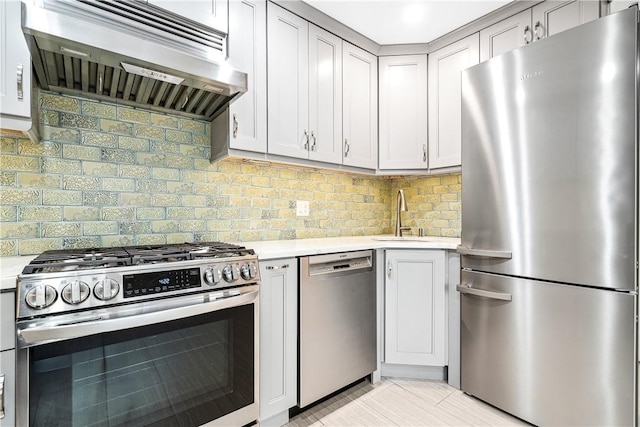 kitchen with gray cabinetry, sink, decorative backsplash, exhaust hood, and appliances with stainless steel finishes