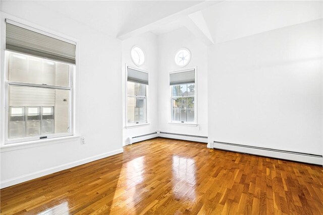 empty room featuring hardwood / wood-style flooring, lofted ceiling, and a baseboard heating unit