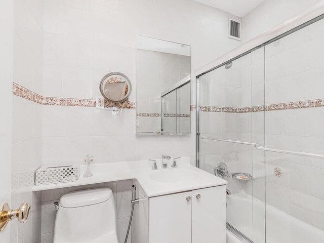 full bathroom featuring shower / bath combination with glass door, vanity, tile walls, and toilet