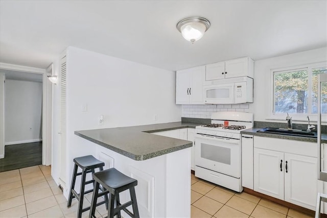 kitchen with a kitchen bar, sink, white cabinets, and white appliances