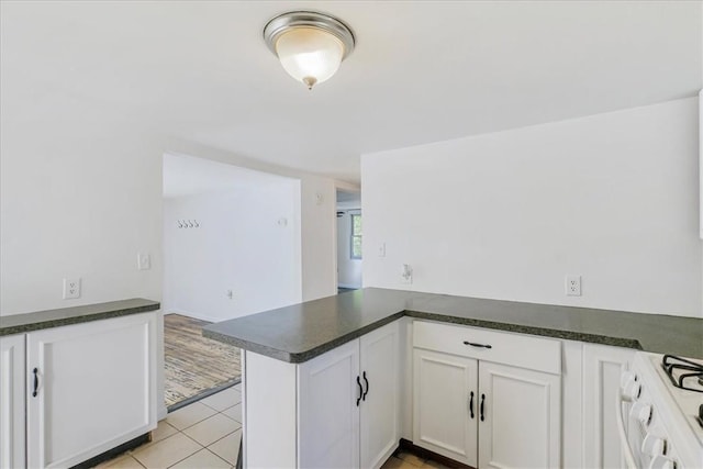 kitchen featuring kitchen peninsula, light tile patterned floors, white range, and white cabinets