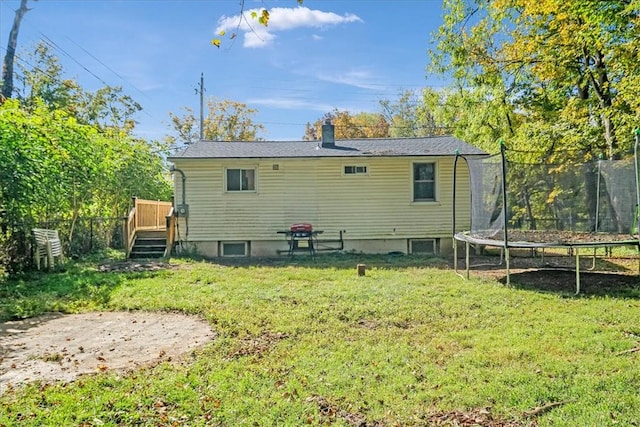 rear view of house with a yard, a trampoline, and a deck