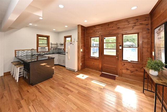 kitchen with white refrigerator with ice dispenser, kitchen peninsula, wooden walls, white cabinets, and light wood-type flooring