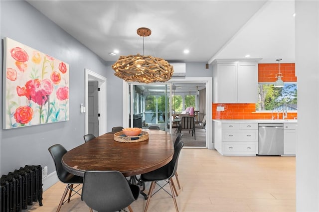 dining space with a wall unit AC, light wood-type flooring, radiator, and a chandelier