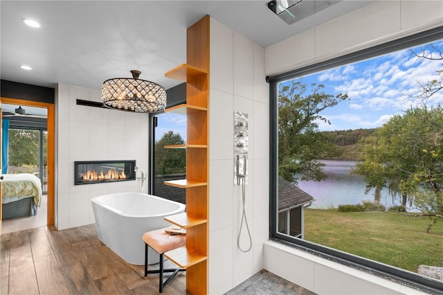 bathroom with hardwood / wood-style floors, a water view, a bathing tub, and a tiled fireplace