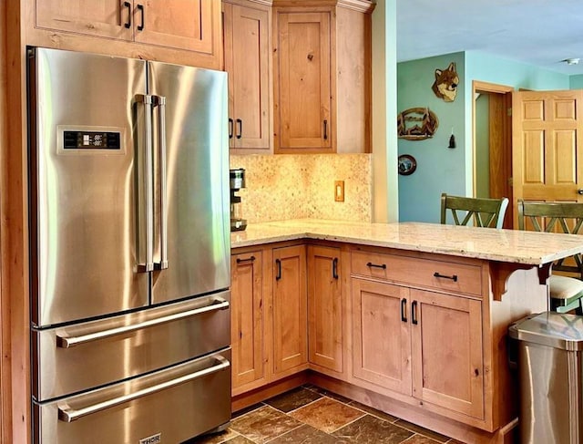 kitchen featuring a kitchen bar, high quality fridge, light stone counters, and kitchen peninsula