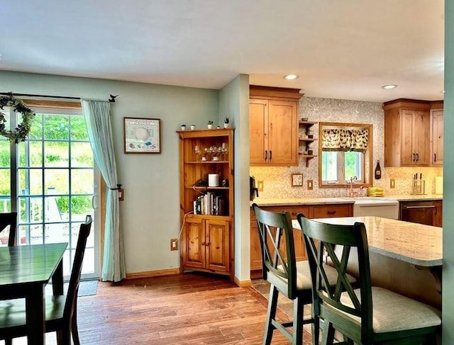 kitchen with dishwasher, light hardwood / wood-style flooring, decorative backsplash, light stone counters, and a breakfast bar area