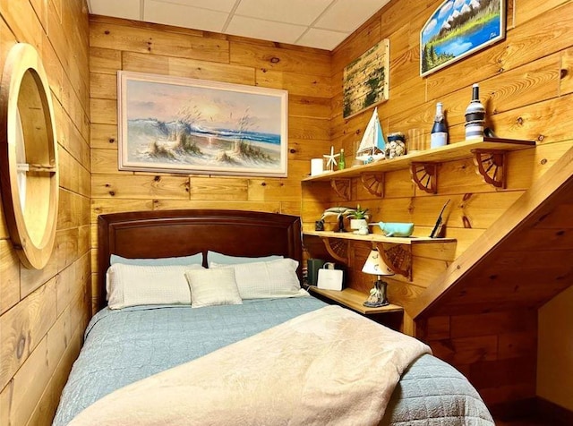 bedroom featuring a paneled ceiling and wood walls