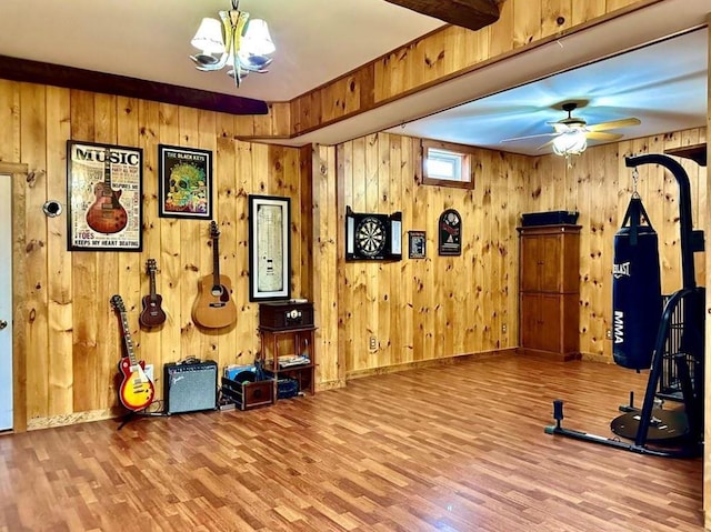 workout room featuring hardwood / wood-style flooring, ceiling fan with notable chandelier, and wood walls