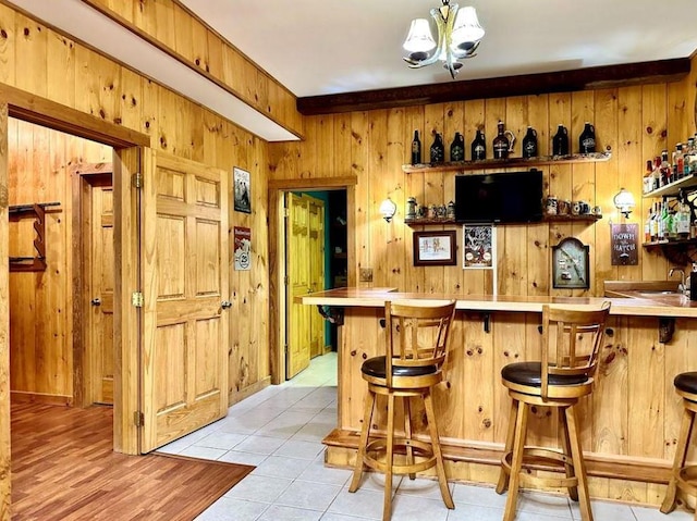 bar featuring a chandelier, light tile patterned floors, beam ceiling, and wood walls