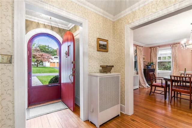 foyer entrance featuring wood-type flooring, ornamental molding, and a notable chandelier