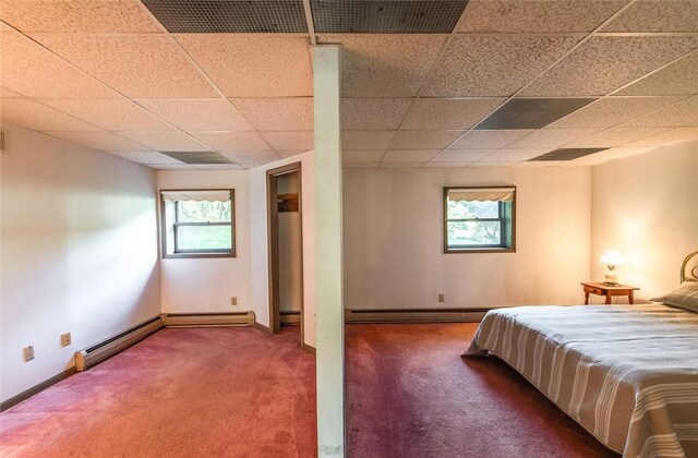 unfurnished bedroom with a drop ceiling, dark carpet, a baseboard radiator, and multiple windows