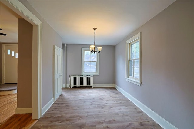 unfurnished dining area featuring light wood-type flooring, radiator, and a chandelier