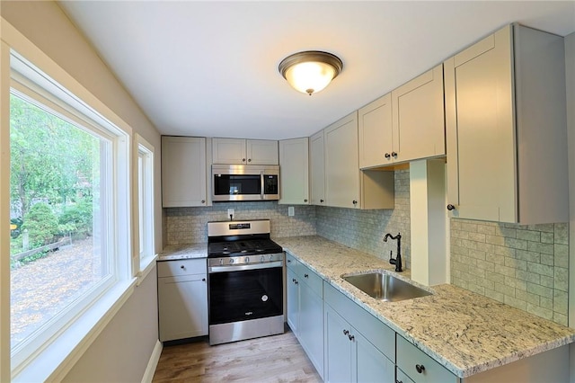 kitchen featuring decorative backsplash, light wood-type flooring, light stone counters, stainless steel appliances, and sink