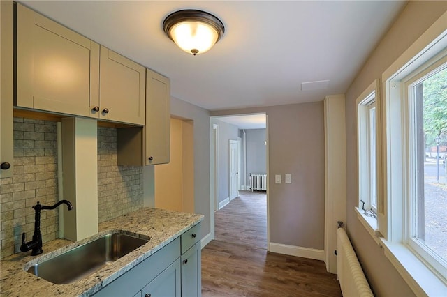 kitchen featuring decorative backsplash, light stone countertops, sink, light hardwood / wood-style flooring, and radiator heating unit