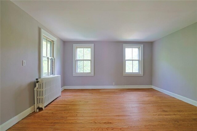 empty room featuring a healthy amount of sunlight, radiator, and light hardwood / wood-style flooring