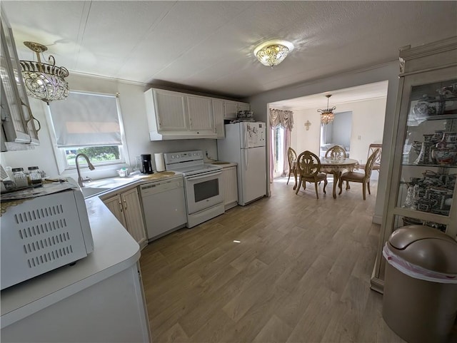 kitchen with white cabinetry, sink, hanging light fixtures, light hardwood / wood-style floors, and white appliances