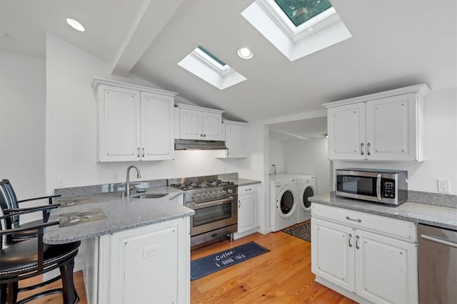 kitchen featuring kitchen peninsula, vaulted ceiling with skylight, separate washer and dryer, appliances with stainless steel finishes, and white cabinetry