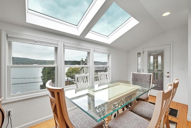 dining room with vaulted ceiling with skylight, a water view, and light hardwood / wood-style flooring