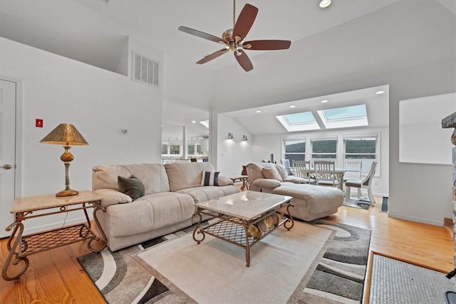 living room with hardwood / wood-style floors, a skylight, high vaulted ceiling, and ceiling fan