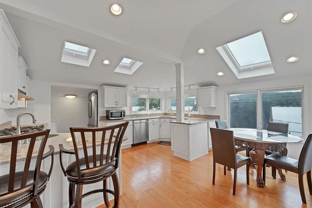 kitchen featuring appliances with stainless steel finishes, lofted ceiling with skylight, white cabinets, a center island, and light hardwood / wood-style floors