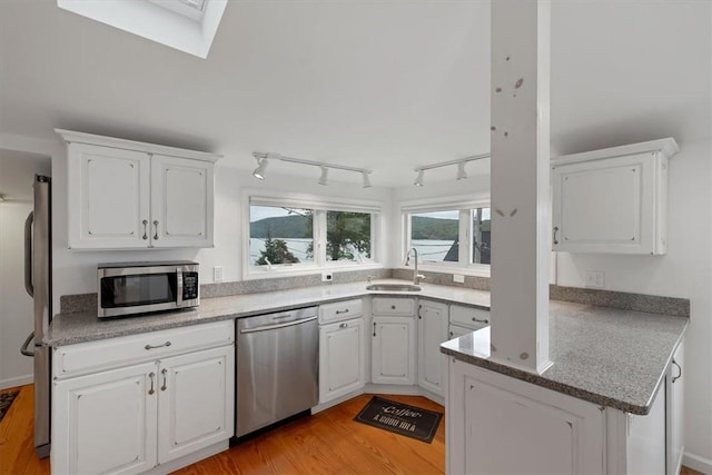 kitchen with a skylight, sink, stainless steel appliances, light hardwood / wood-style flooring, and white cabinets