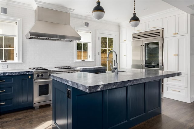 kitchen featuring wall chimney exhaust hood, blue cabinets, a kitchen island with sink, pendant lighting, and high quality appliances