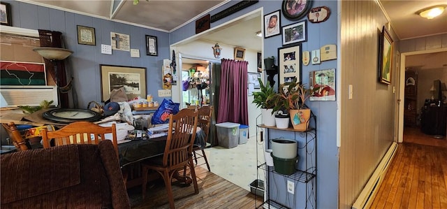 dining space featuring hardwood / wood-style flooring, ornamental molding, baseboard heating, and wooden walls