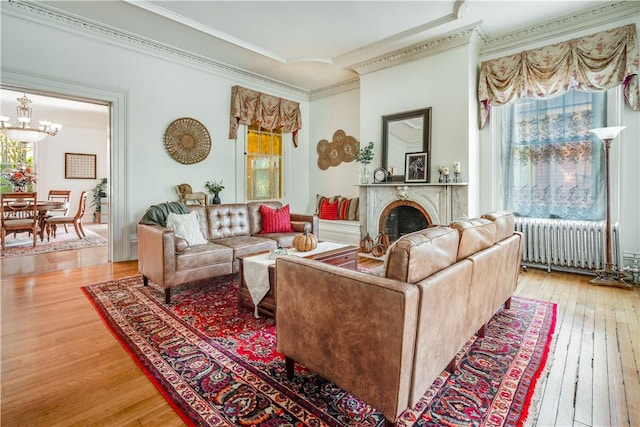 living room with light wood-type flooring, radiator, ornamental molding, and a notable chandelier