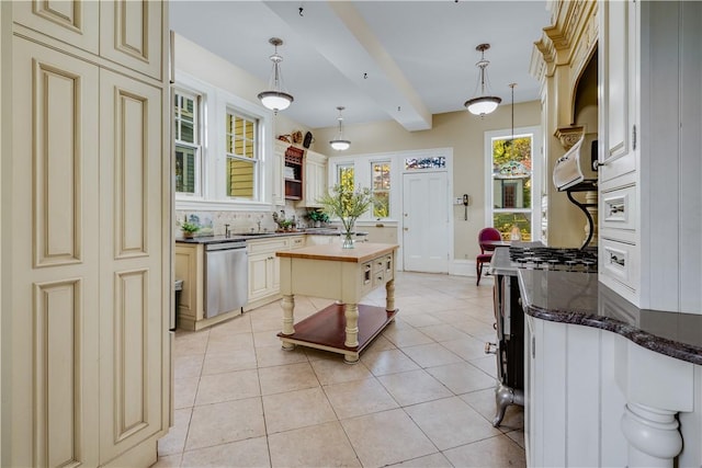 kitchen featuring stainless steel dishwasher, hanging light fixtures, cream cabinetry, and beamed ceiling