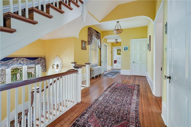 hallway with lofted ceiling, wood-type flooring, and radiator heating unit