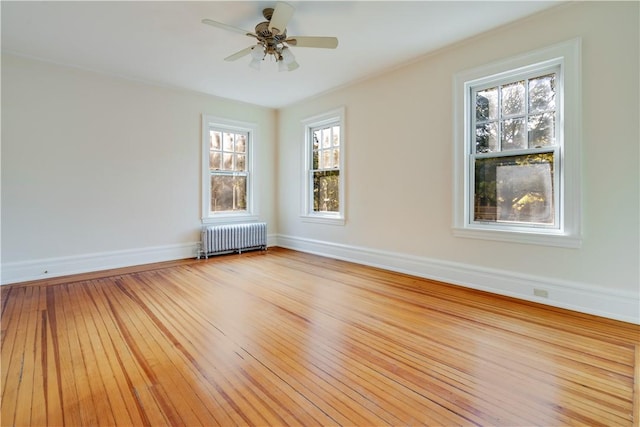 empty room with ceiling fan, radiator heating unit, plenty of natural light, and light wood-type flooring