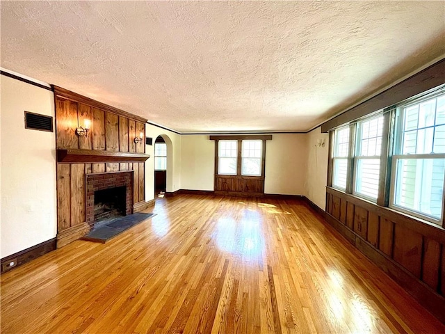 unfurnished living room featuring a fireplace, a textured ceiling, light hardwood / wood-style floors, and ornamental molding