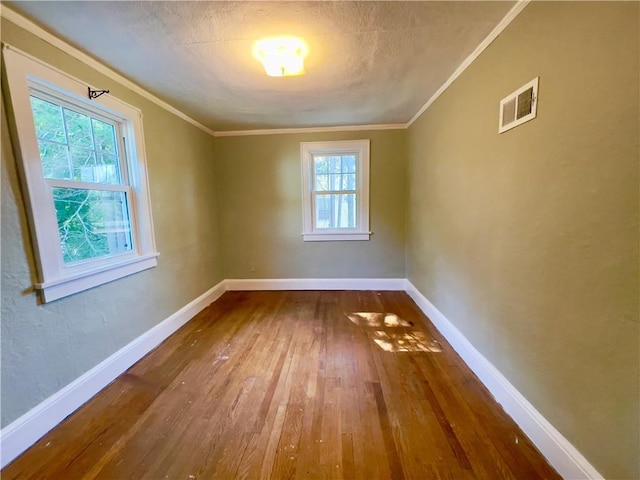 empty room with a wealth of natural light, crown molding, and wood-type flooring