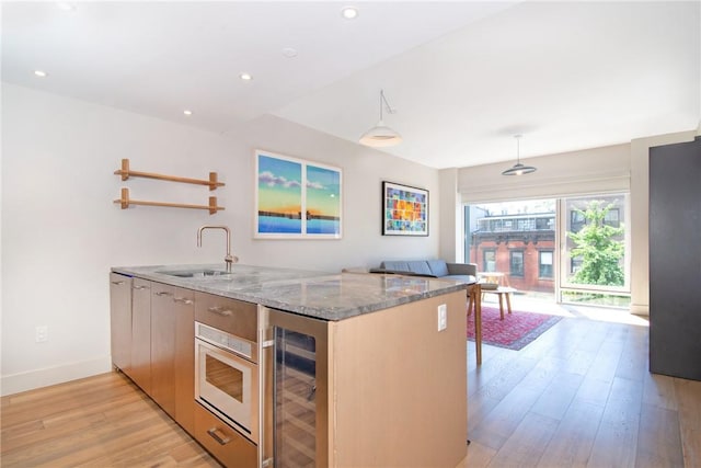 kitchen with kitchen peninsula, light wood-type flooring, light stone counters, sink, and wine cooler