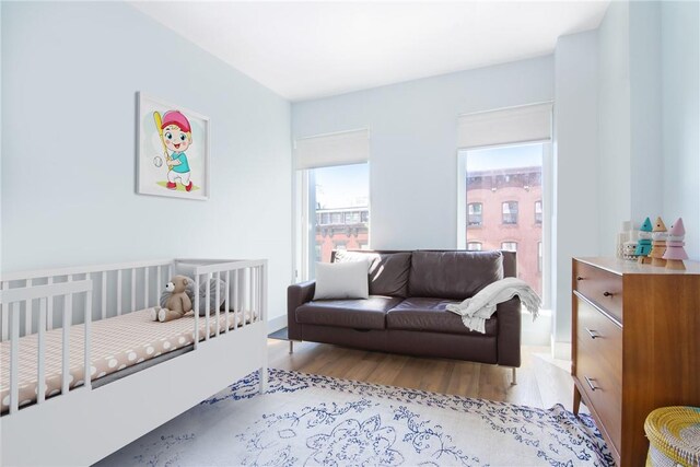 bedroom featuring multiple windows, light hardwood / wood-style flooring, and a nursery area