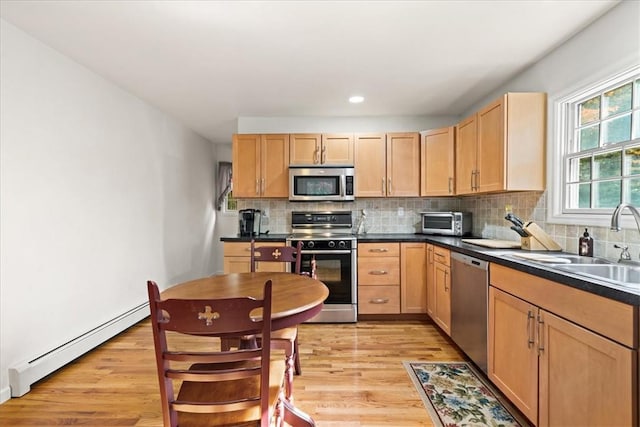 kitchen featuring backsplash, stainless steel appliances, a baseboard heating unit, light brown cabinets, and light hardwood / wood-style floors