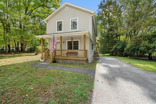 traditional-style home featuring aphalt driveway, covered porch, and a front yard