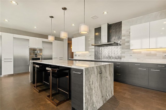 kitchen with white cabinetry, wall chimney range hood, pendant lighting, decorative backsplash, and a kitchen island