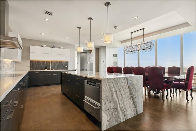 kitchen featuring white cabinetry, a center island, wall chimney range hood, light stone counters, and pendant lighting