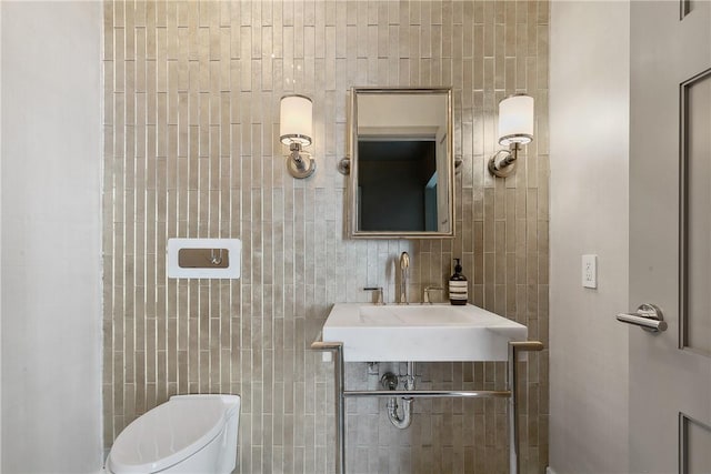 bathroom with toilet, tile walls, and sink